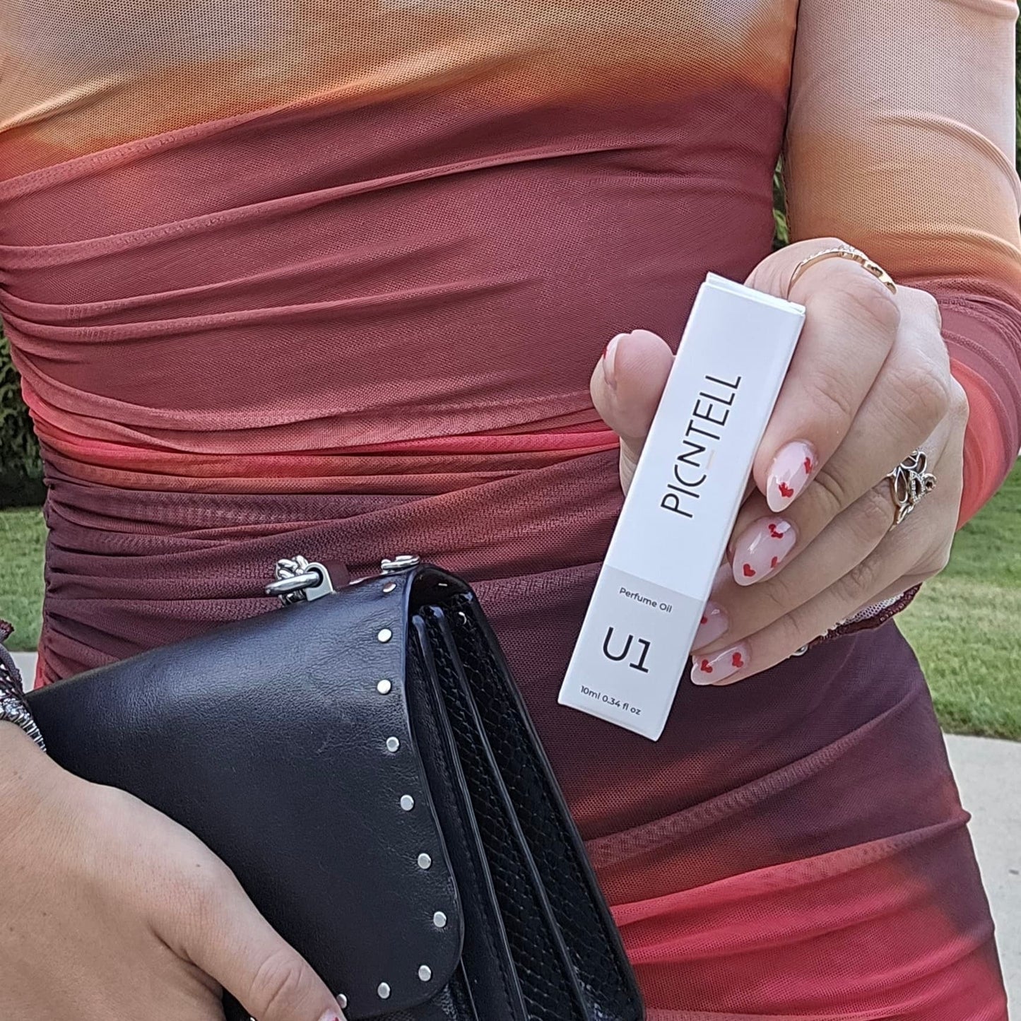 U1 perfume oil box held in hand near black handbag.