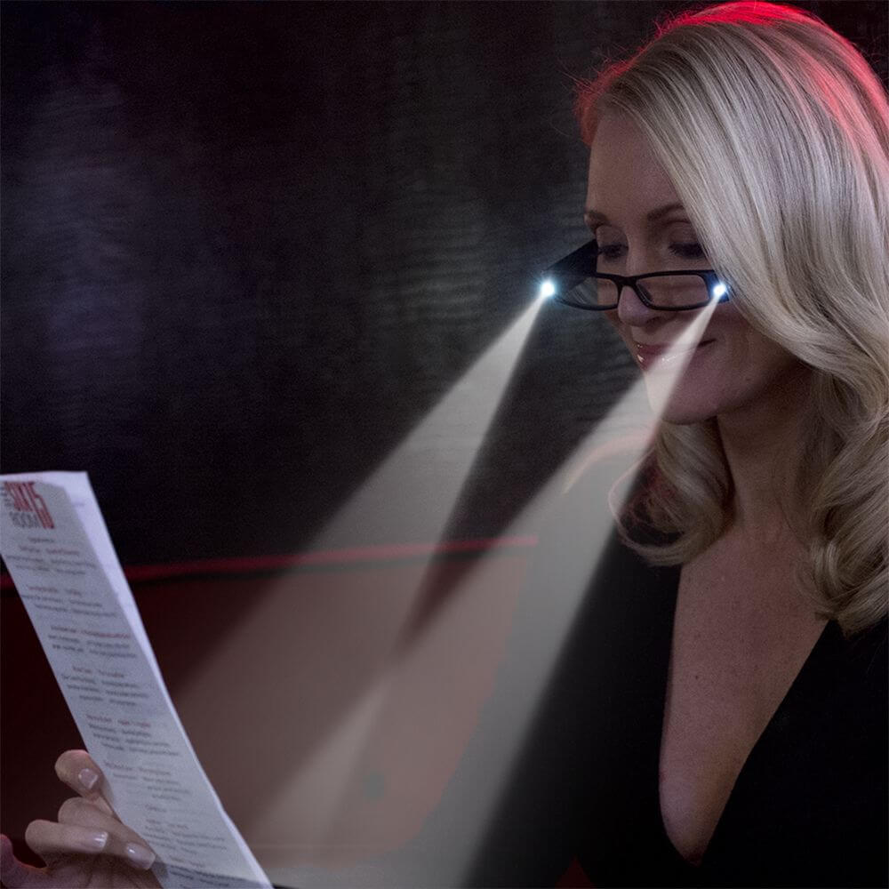 Lighted reading glasses worn on a person, dark frames with bright LED light over the lens