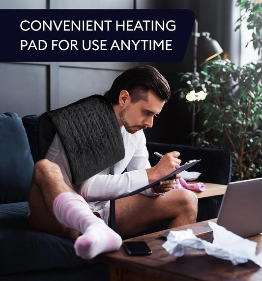 Black heating pad with controller in hand while a person reclines on a sofa