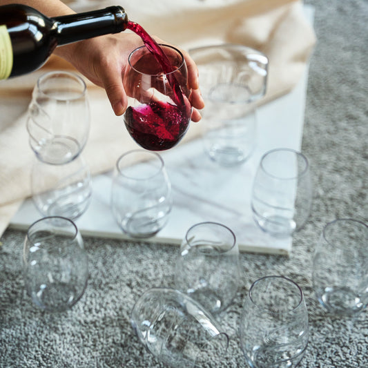 Stemless acrylic wine glass with finger-indented bowl, red wine being poured