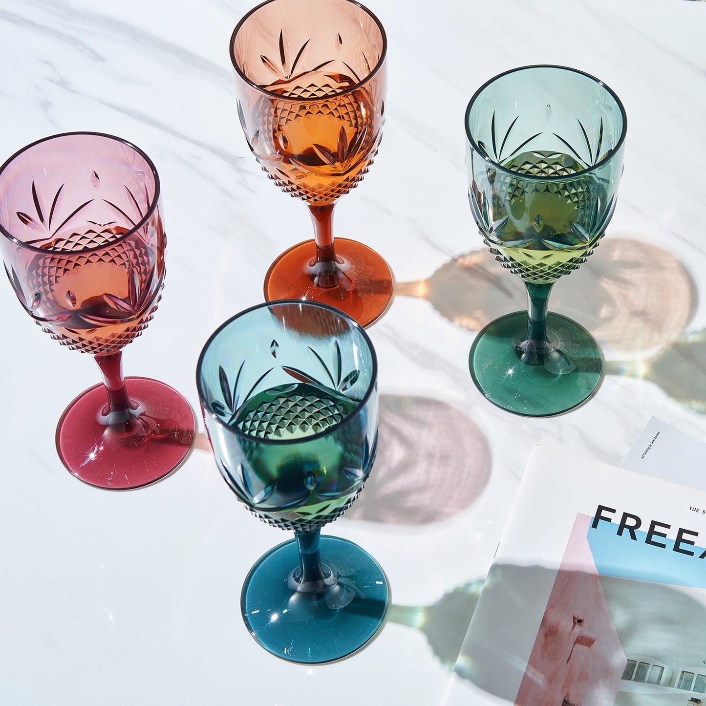 Set of four stemmed wine glasses with faceted bowls in orange, pink, teal, and green