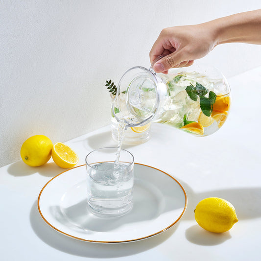 Acrylic pitcher with lid being poured; transparent container with lemon and mint leaves.