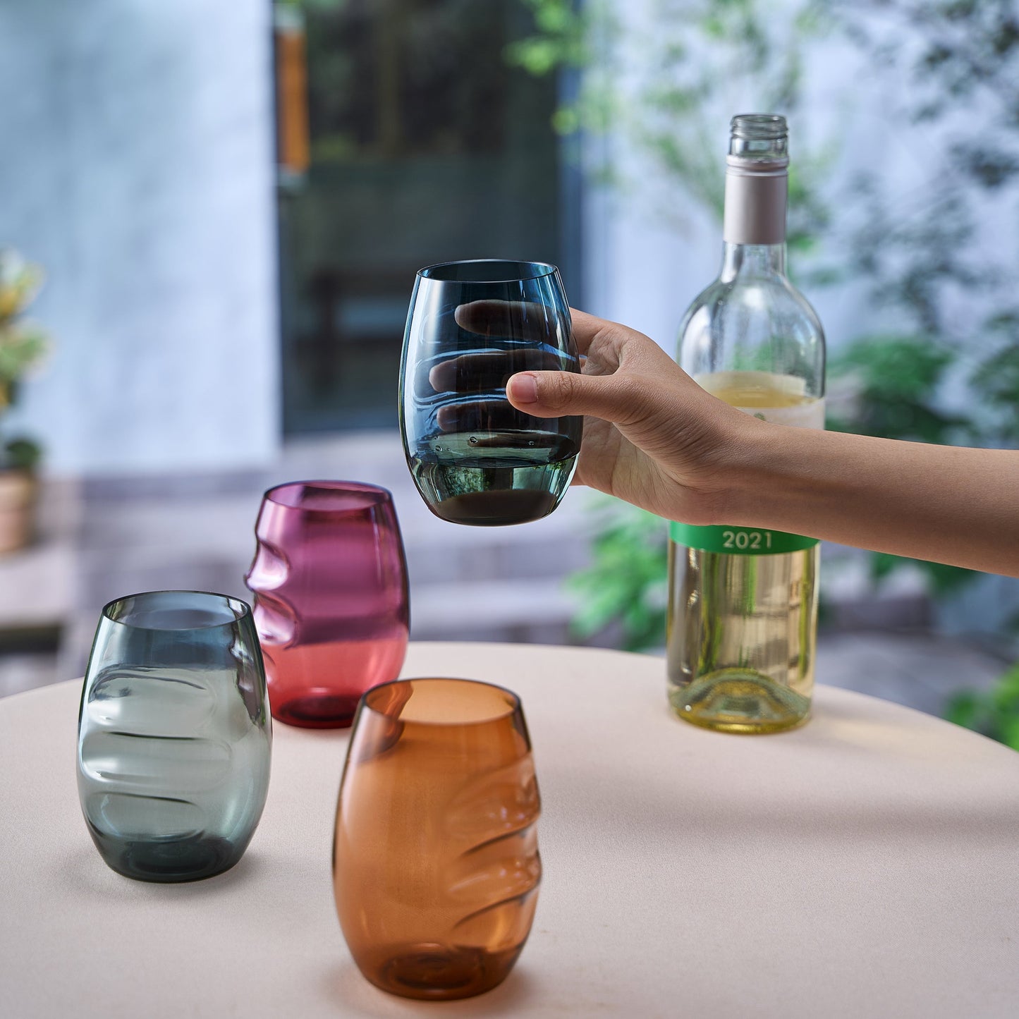 Finger-indented stemless acrylic wine glass, clear teal tint, held in hand