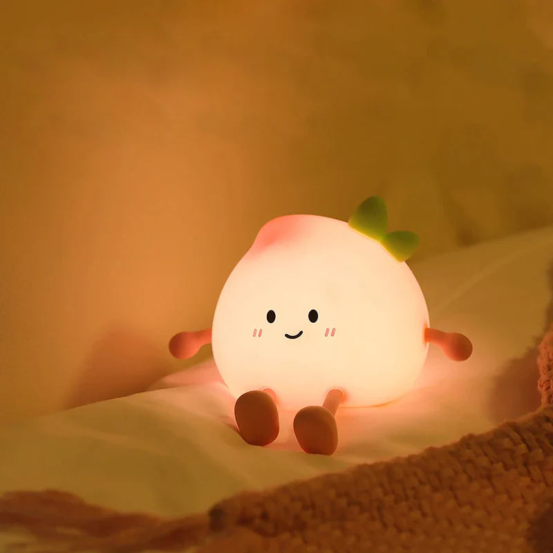 Warm glowing peach-shaped night light with smiling face and green leaf on bedding