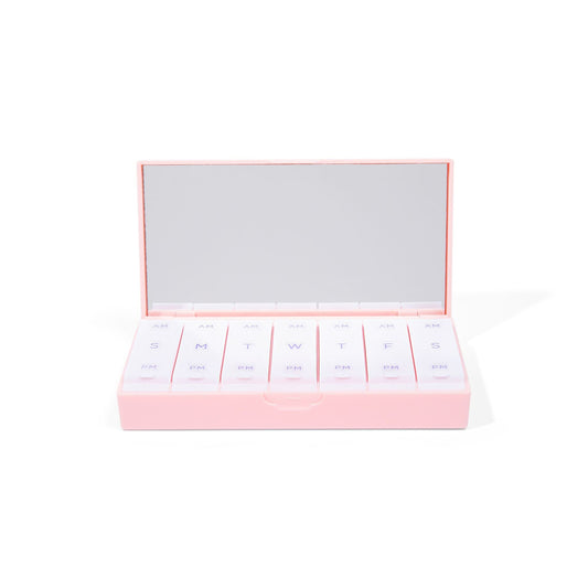 Blush pink AM/PM pill box open lid with row of labeled pill compartments
