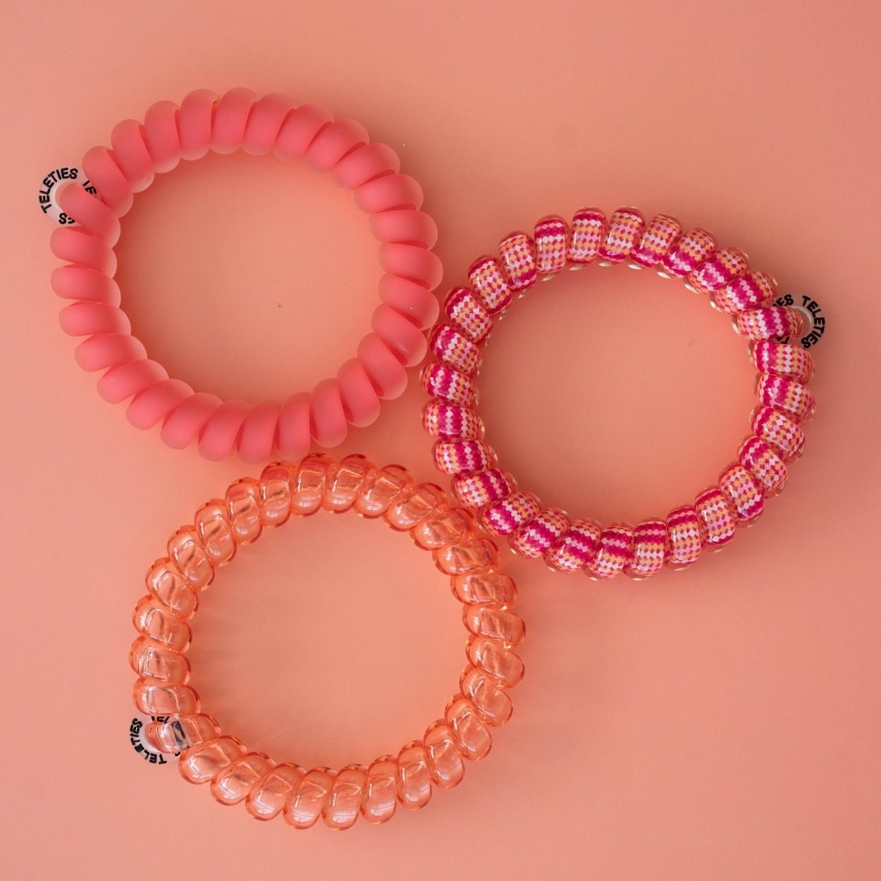 Set of three large hair ties: solid coral, pink check, and translucent pink