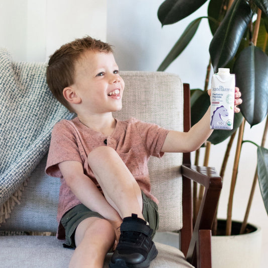 Child holding a Kate Farms Pediatric Peptide 1.0 strawberry formula carton, 8.45 fl oz.