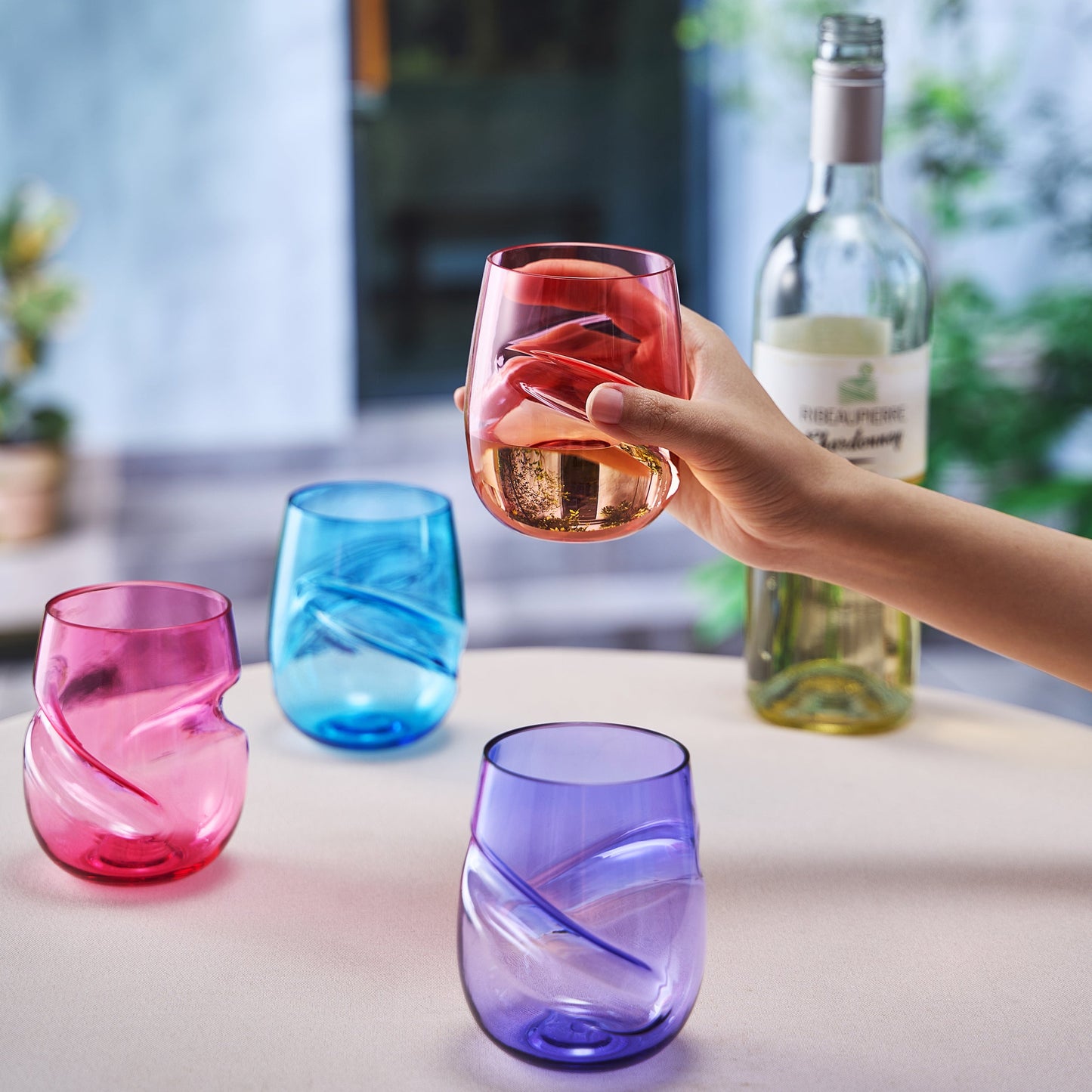 Stemless acrylic wine glasses set of 4 with finger-indent cups, held in coral with pink, blue, purple