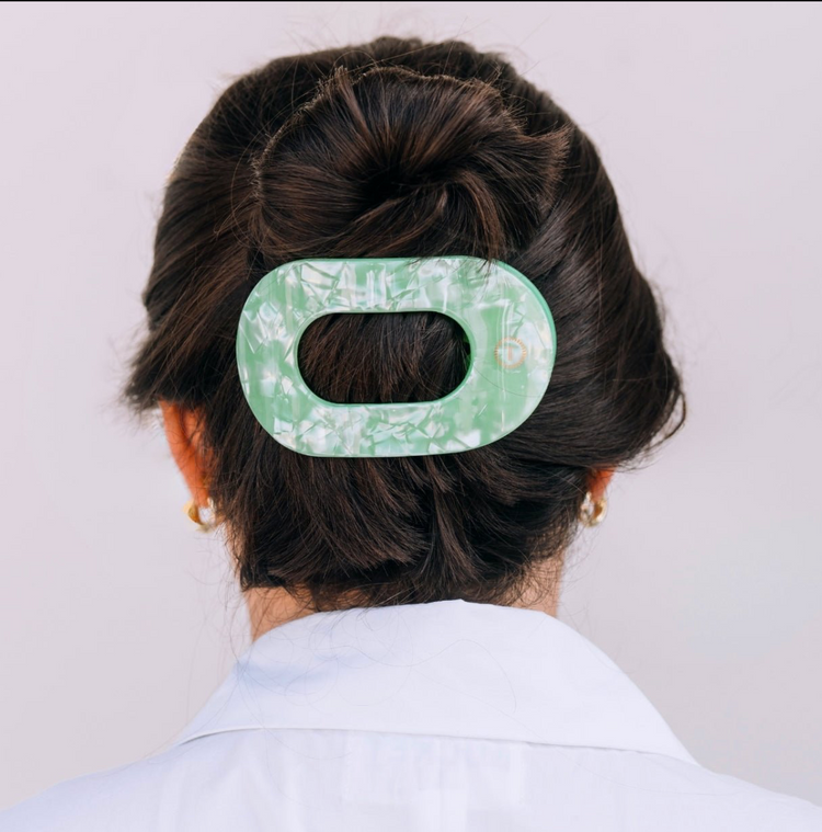Floral green hair clip on the back of a women's head who has brown hair.