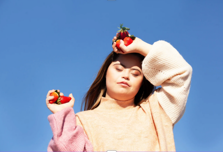 Business founder with Down syndrome standing in the sun with her eyes closed, holding berries