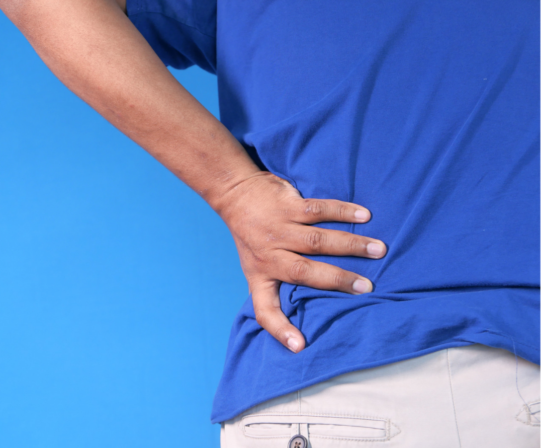 A person is gripping their lower back to show it is in pain. They are wearing a blue t-shirt agaisnt a blue background