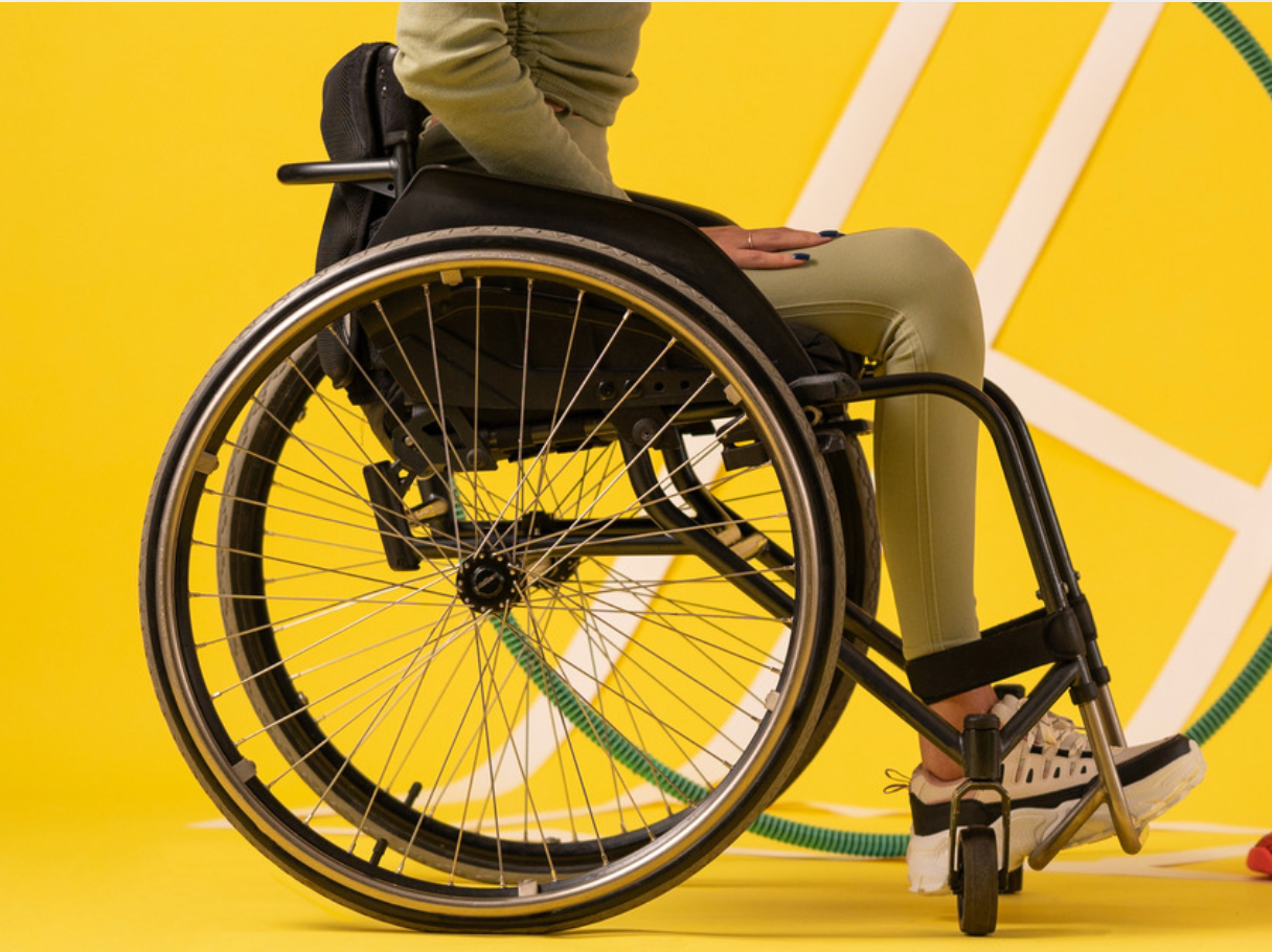 Side view of a person in a manual wheelchaiir with a bright yellow background