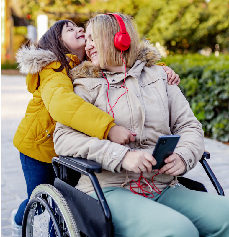 A mom using a manual wheelchair wearing read headphones, it hugged from behind by her 10-year-old daugter in a yellow jacket