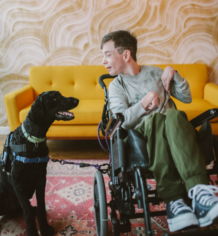 Man in wheelchair and his black service dog looking at each other and smiling
