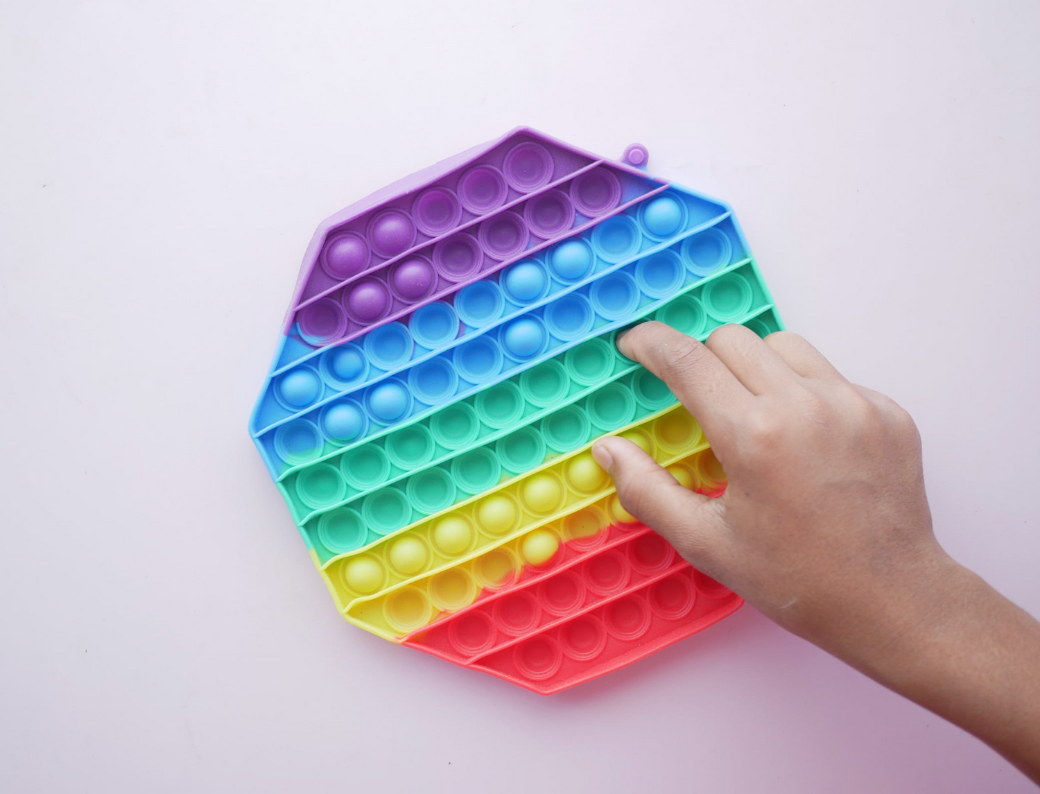 Hand pressing on a dot on a rainbow colored fidget toy on a purple background