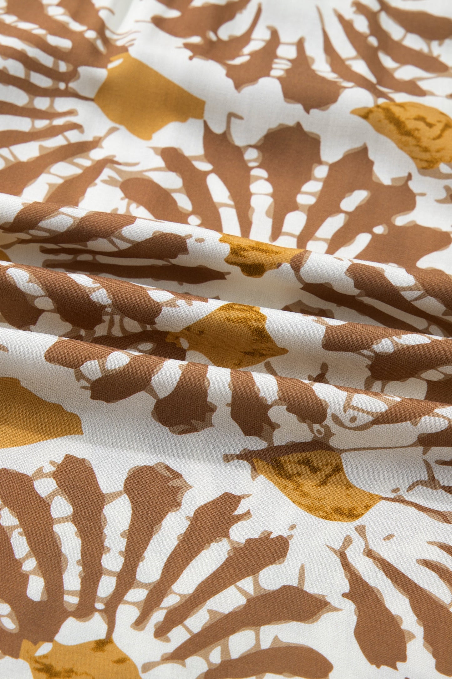 Abstract printed fabric on a loose long plus dress in white, tan, and yellow tones.