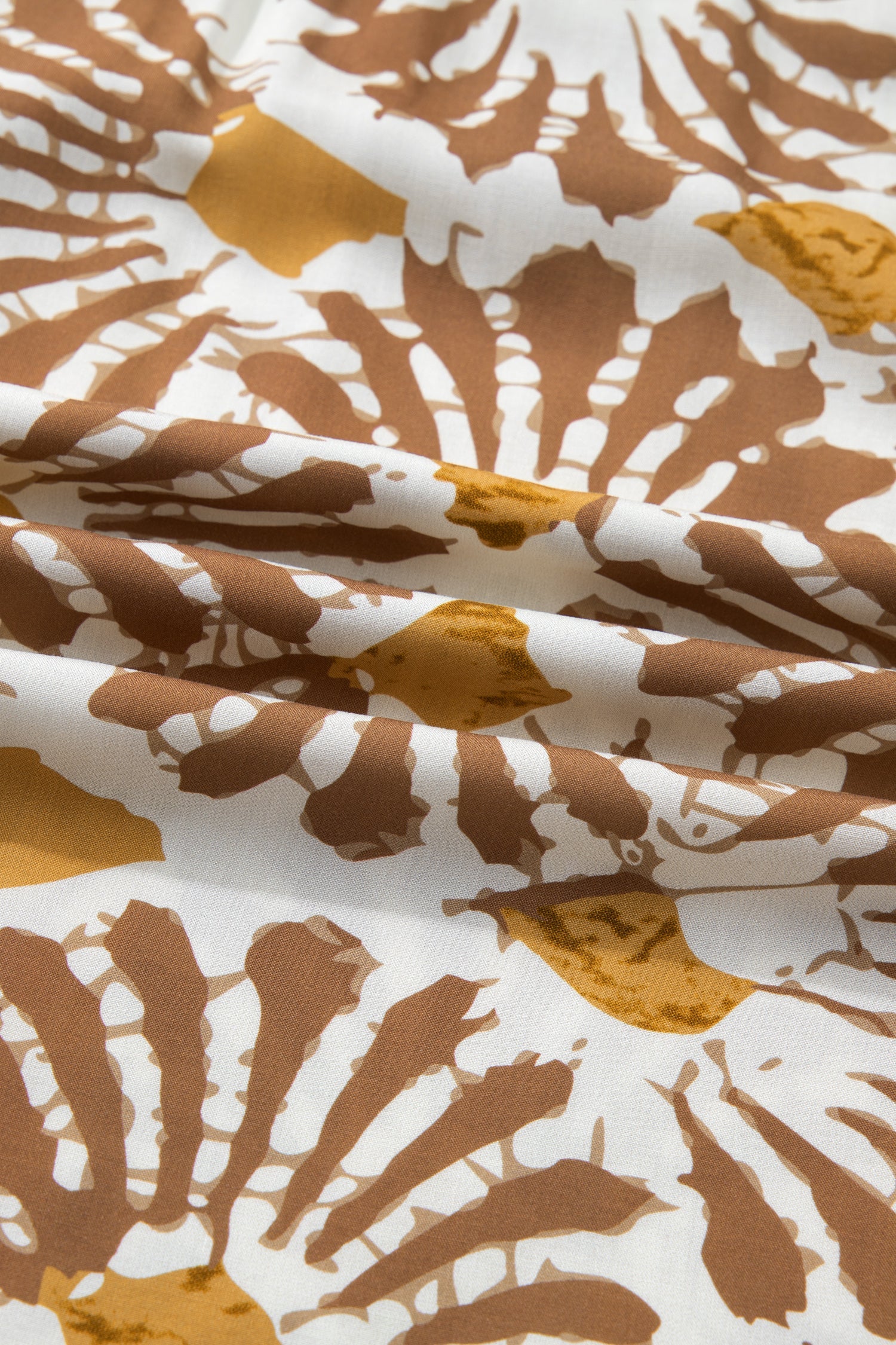 Abstract printed fabric on a loose long plus dress in white, tan, and yellow tones.