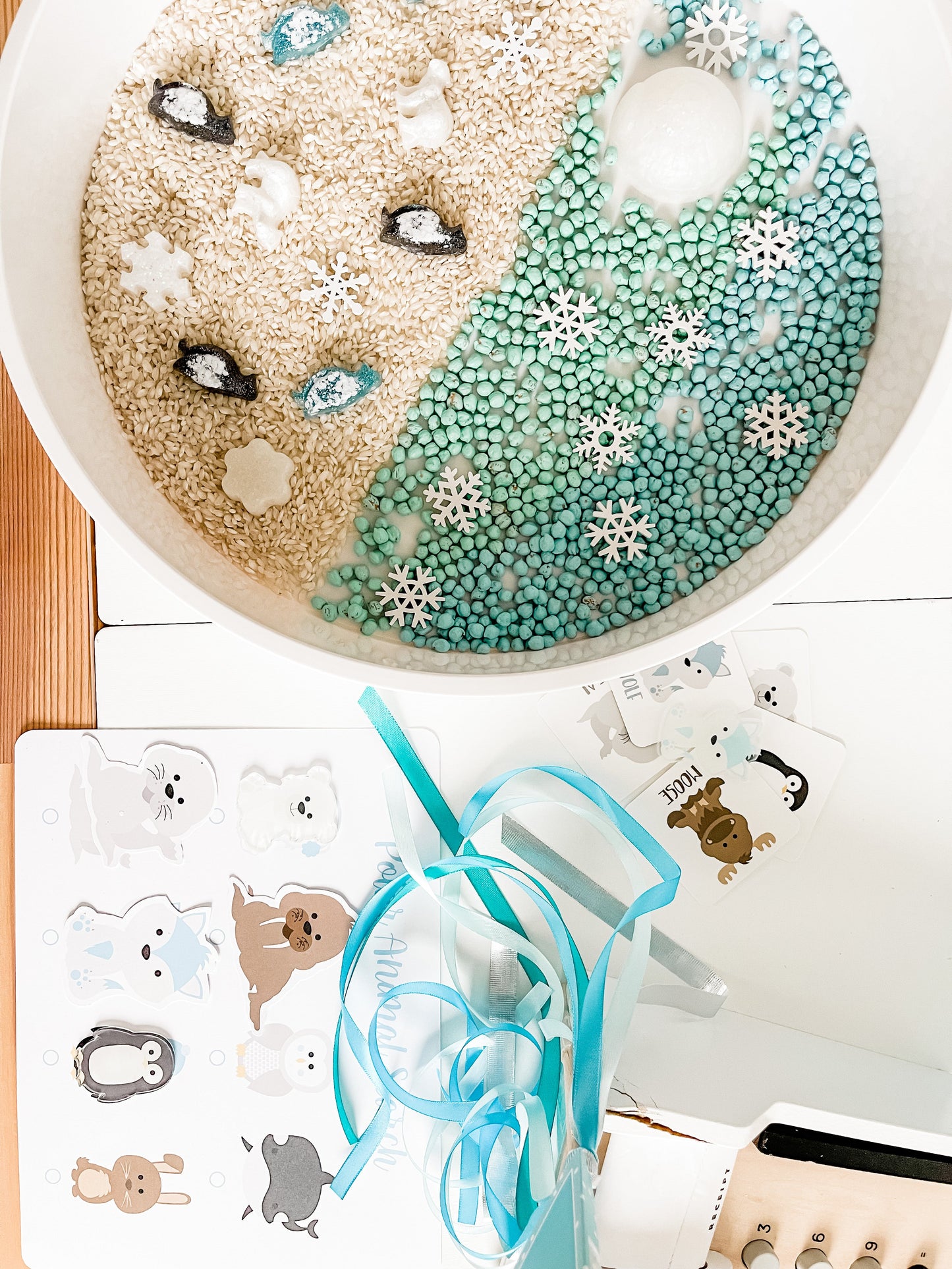 Polar animal sensory bin section with white and teal beads and snowflake-decor foam pieces