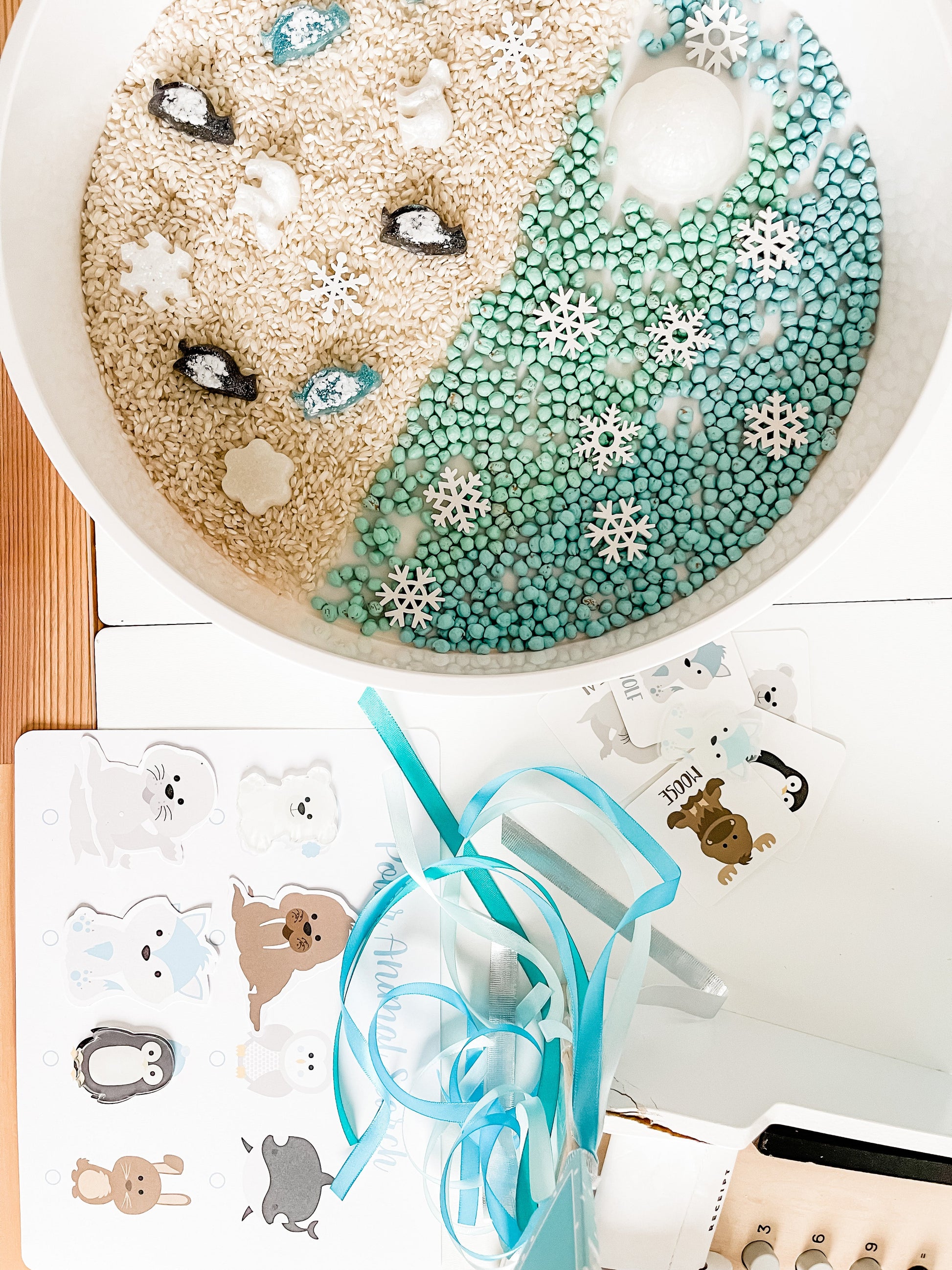 Polar animal sensory bin section with white and teal beads and snowflake-decor foam pieces