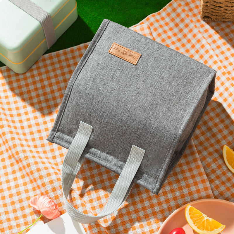 Insulated lunch bag in light gray with top handles and tan logo label patch