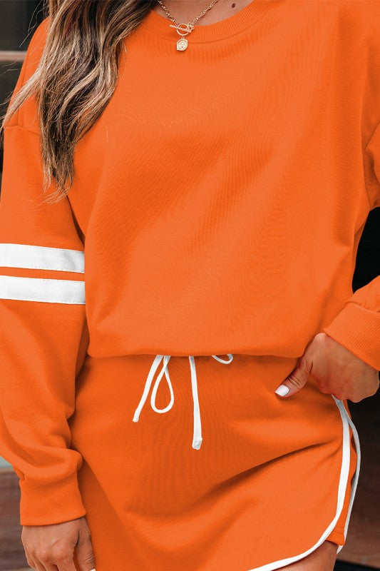 Orange pullover with white stripe cuff and matching mini skirt with white drawstring.