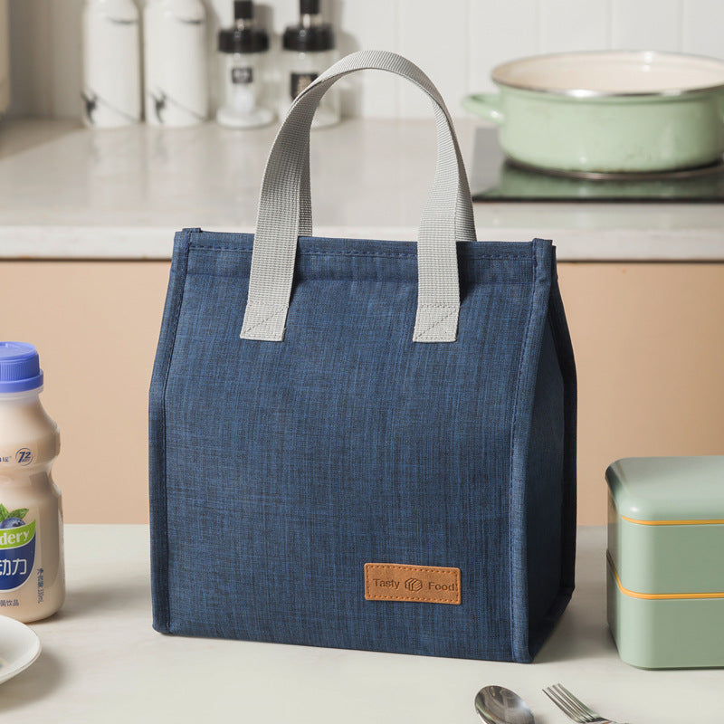 Blue insulated lunch bag with light gray handles and tan logo label patch
