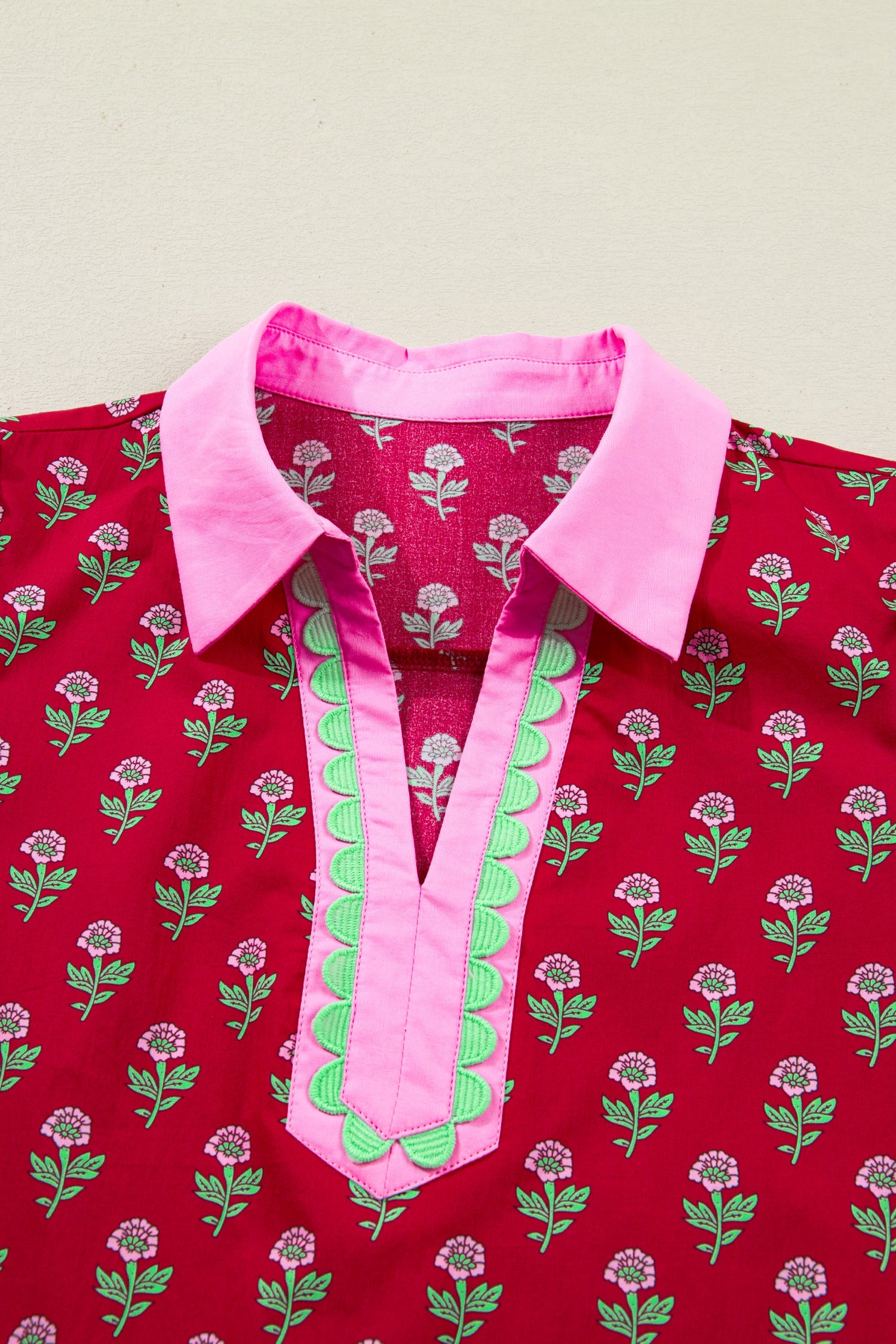 Close-up of red dress neckline with pink collar and V-shaped decorative trim over print.