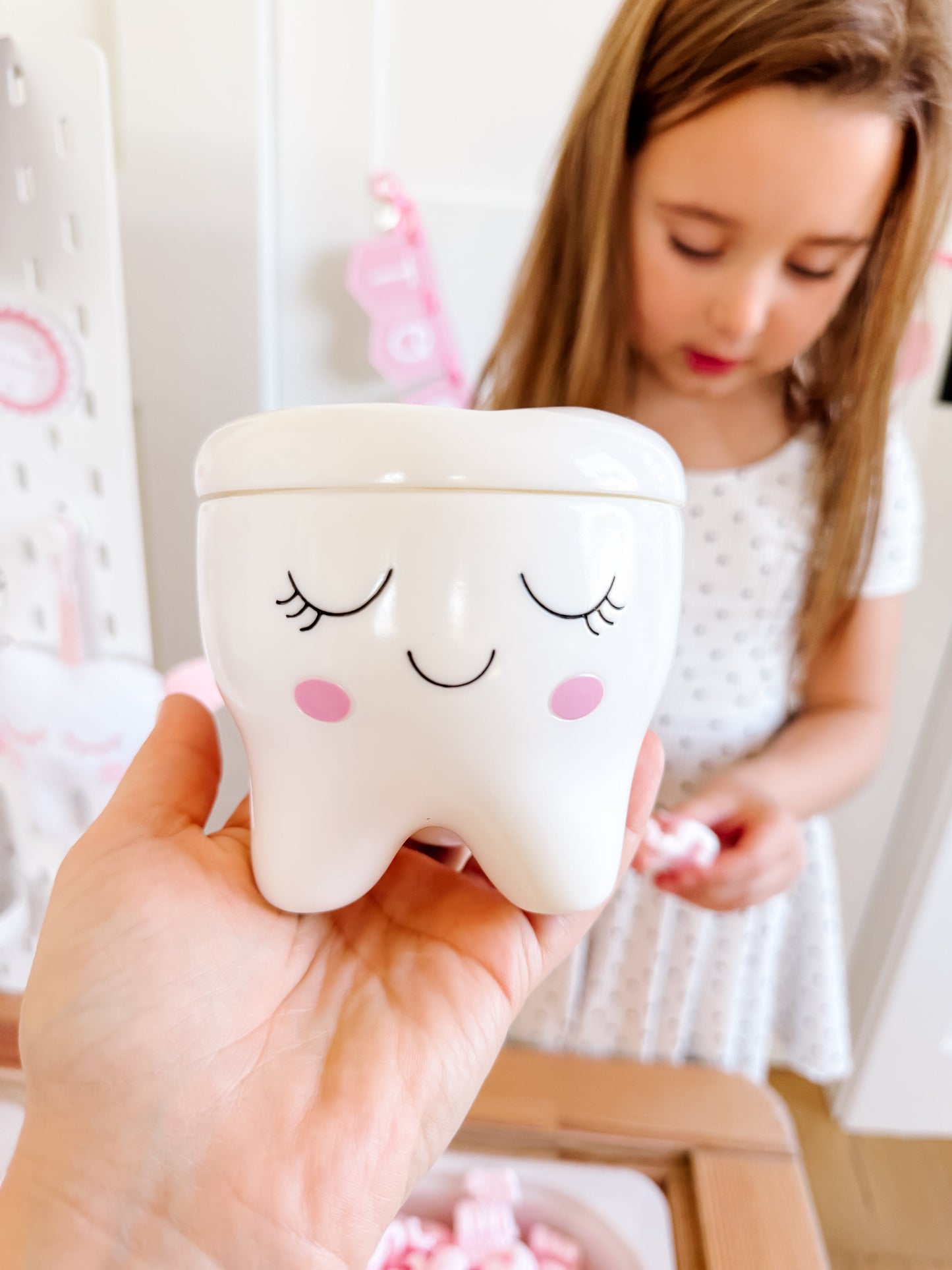 Tooth-shaped ceramic box with closed-eye smile and pink cheeks, held toward camera