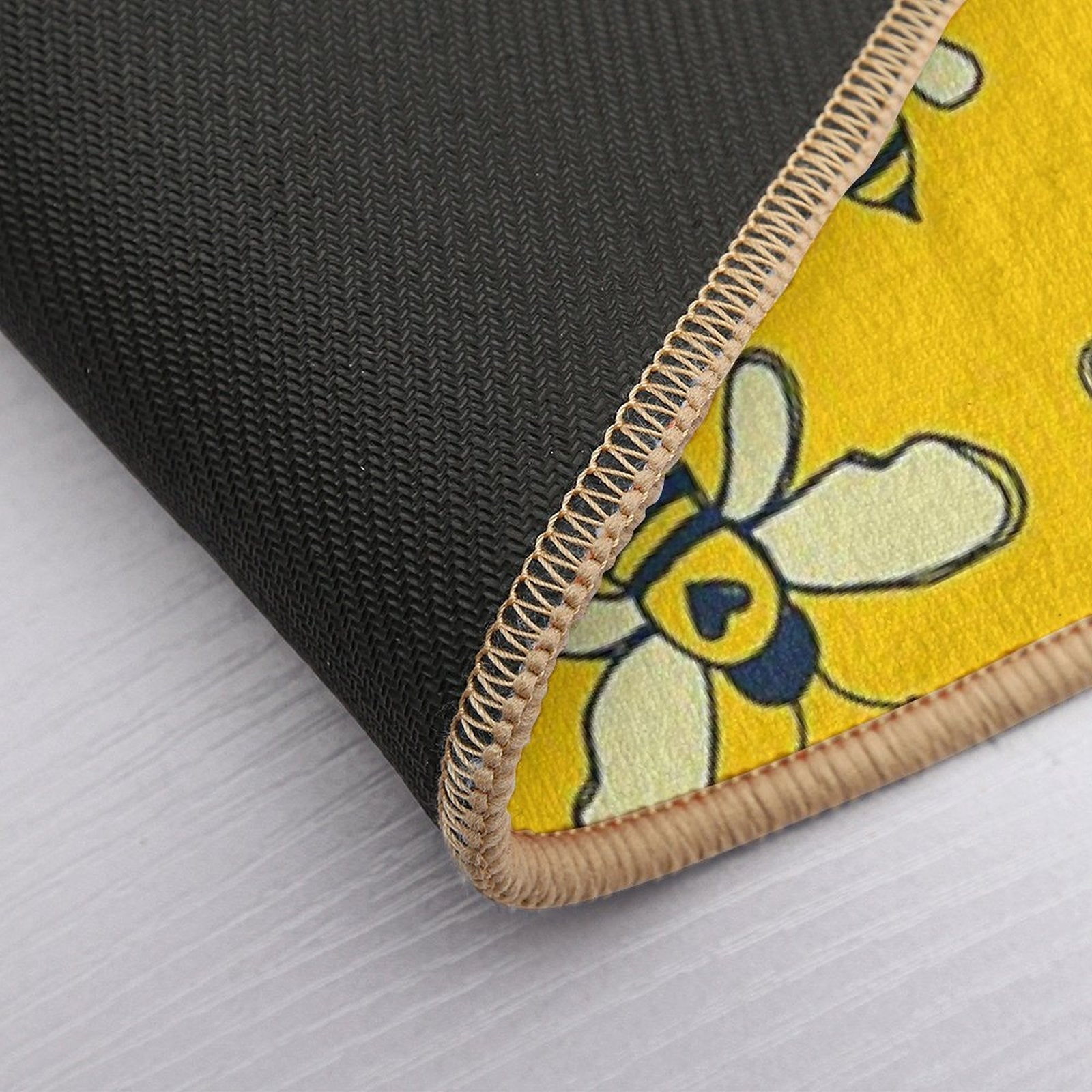 Corner of yellow bee bath mat showing stitched edge and dark textured backing