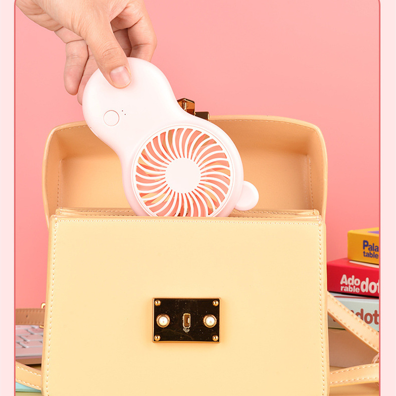 Pink handheld pocket mini fan with round grille and bear ears, clipped near an open bag