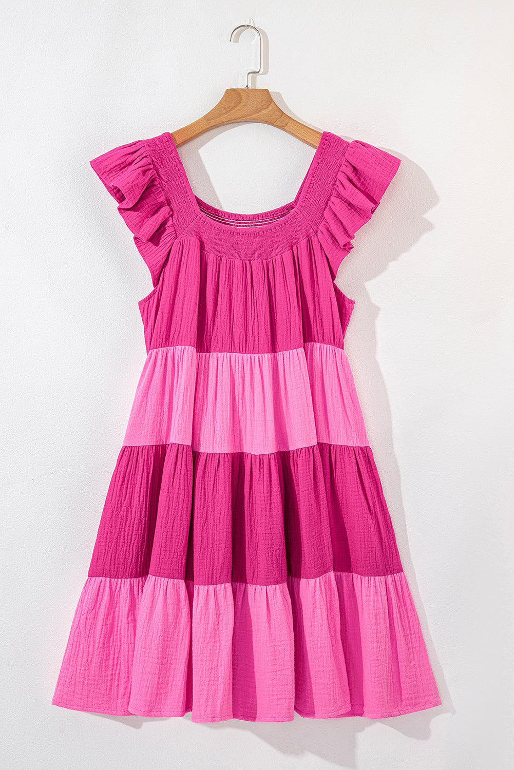 Pink tiered mini dress on a hanger with ruffled flutter sleeves and scoop back