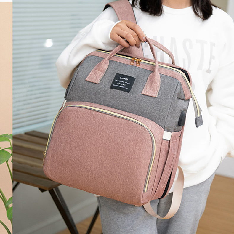 Baby crib backpack, gray and mauve with front zipper and top handle, carried by person