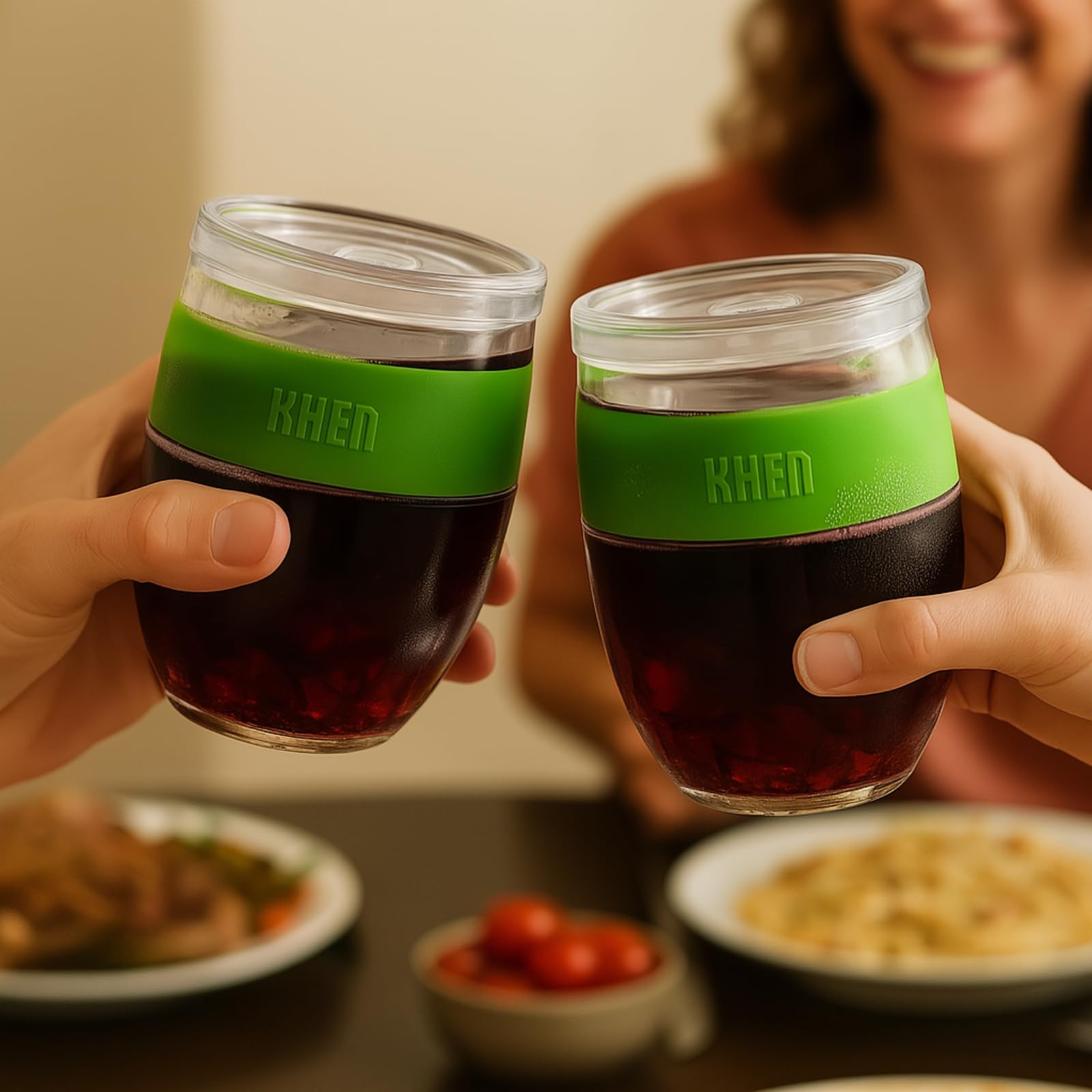 Two stemless acrylic wine glasses held by hands, green band, clear body with red wine