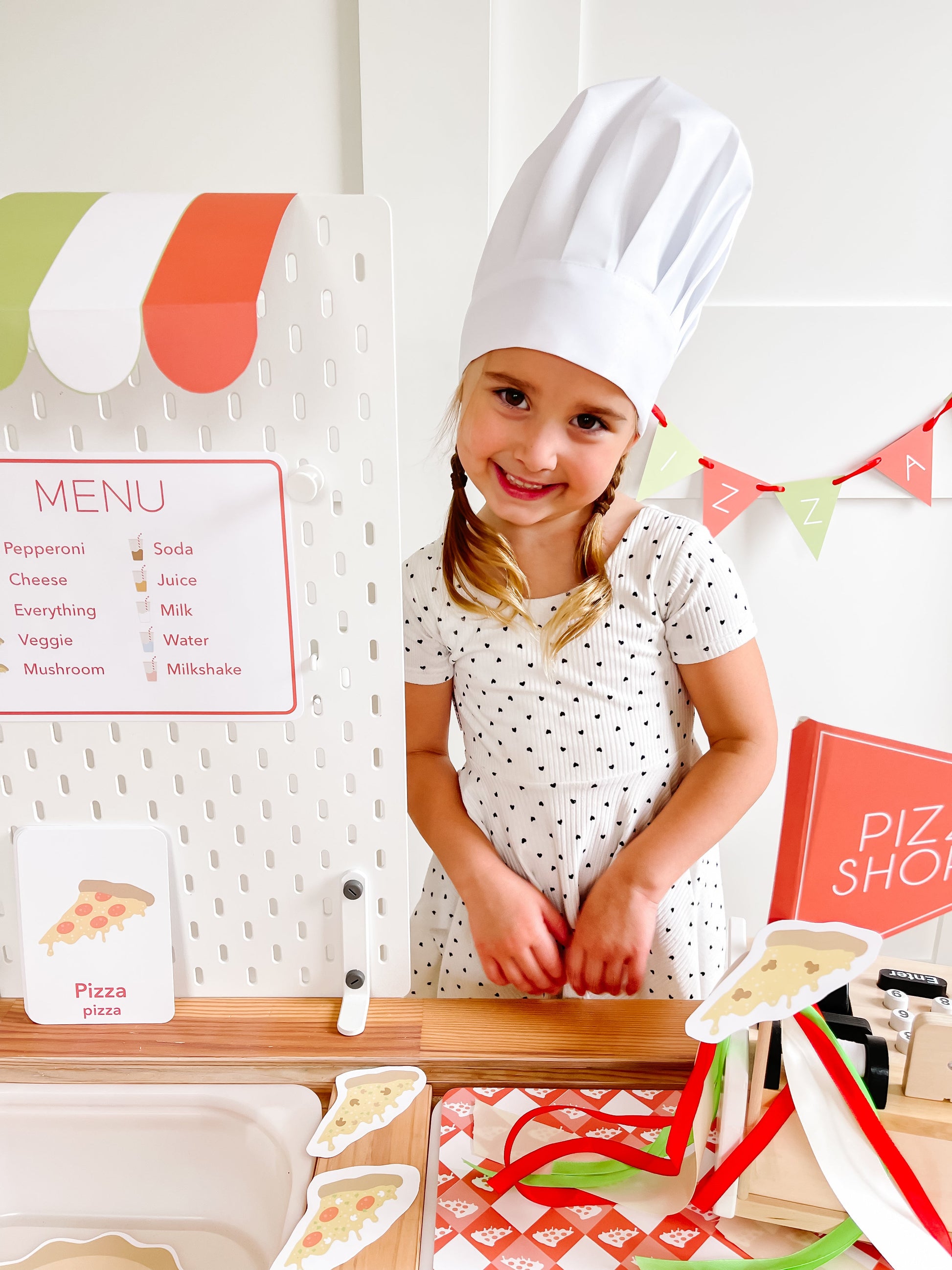 Pizza shop play kit with menu board, child in white chef hat, and pizza graphics