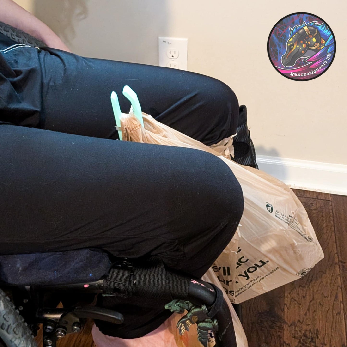 Light blue/teal wheelchair bag hook supporting a shopping bag for hands-free carry