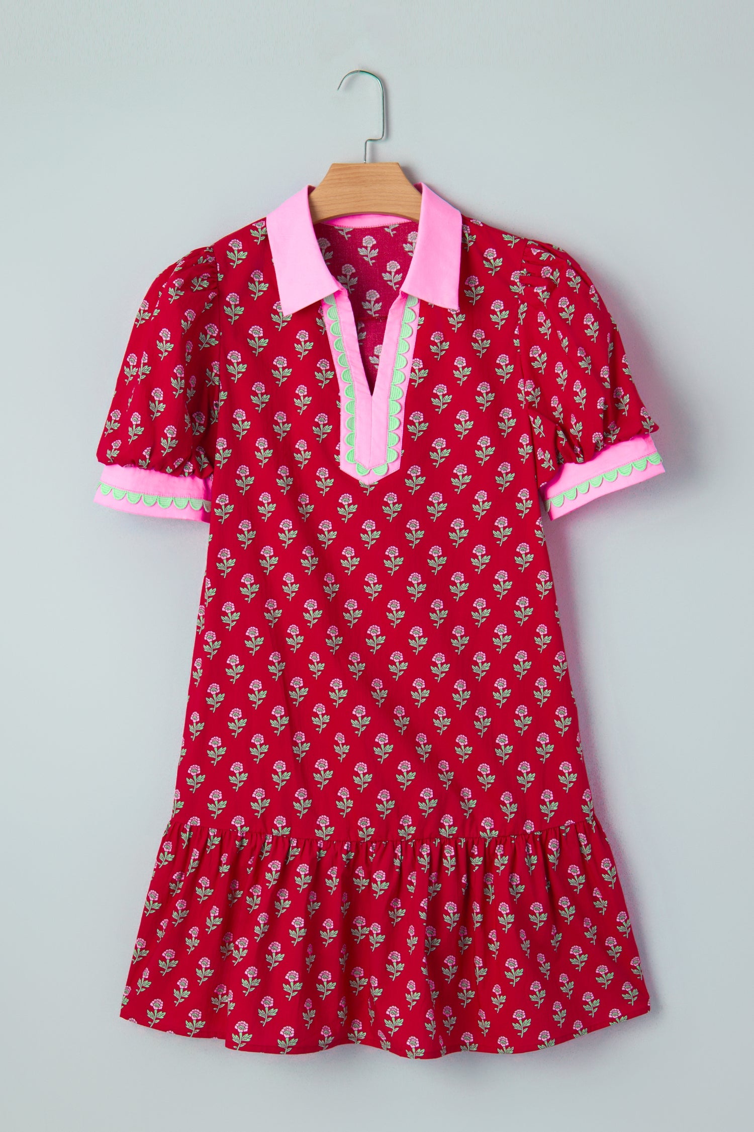 Red mini dress hanging on a hanger with pink collar trim and patterned puff sleeves.