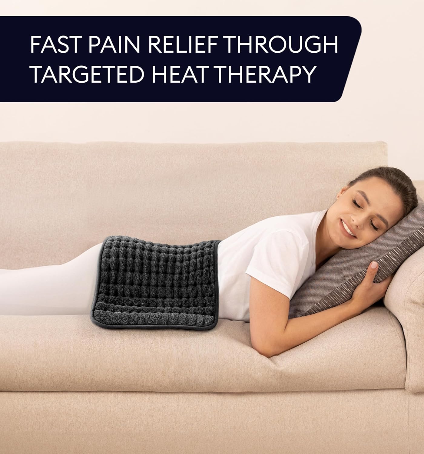 Black heating pad laid across a sofa for targeted back heat with controller cord