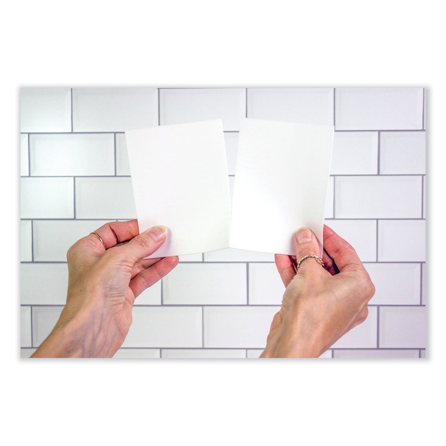 Laundry detergent sheets held in hands, showing thin white dissolvable pieces