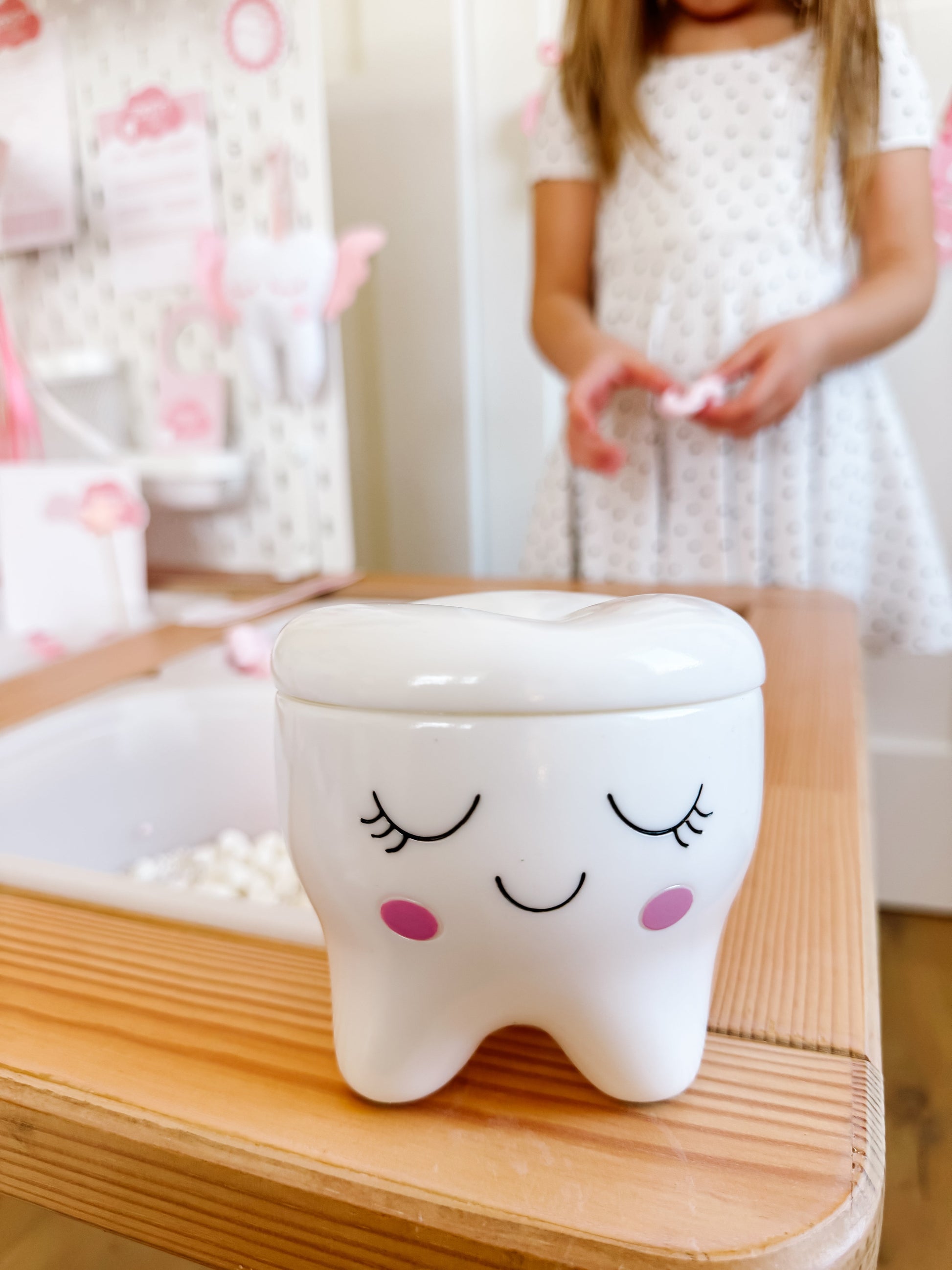 Tooth-shaped ceramic box with smiling face, held by a child in a white dress