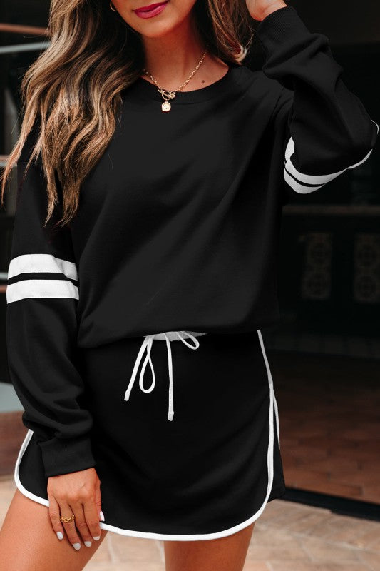 Black pullover and mini skirt set with white drawstring ties and white striped sleeve detail.