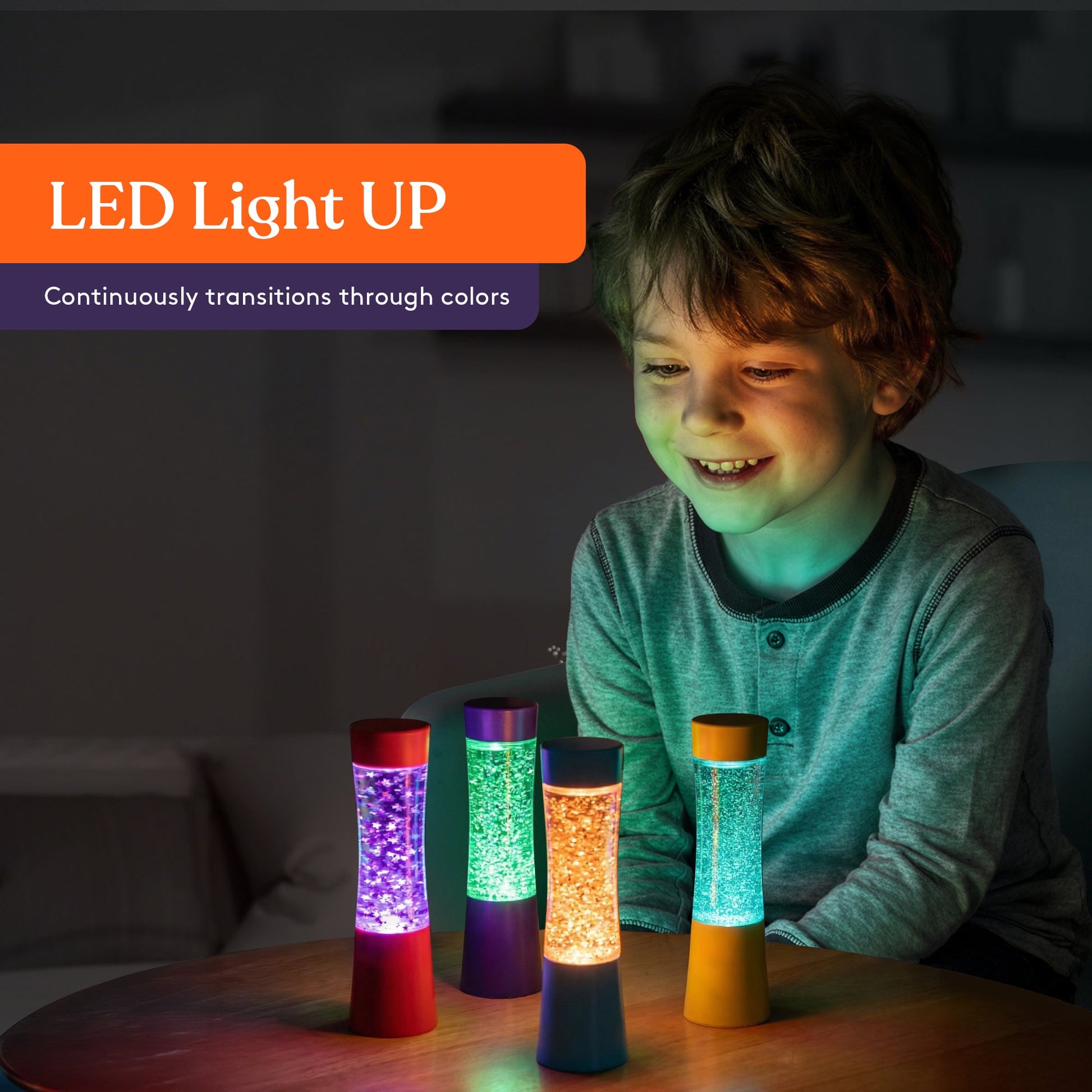 Four light-up glitter sensory tubes glowing on a tabletop, held by a child