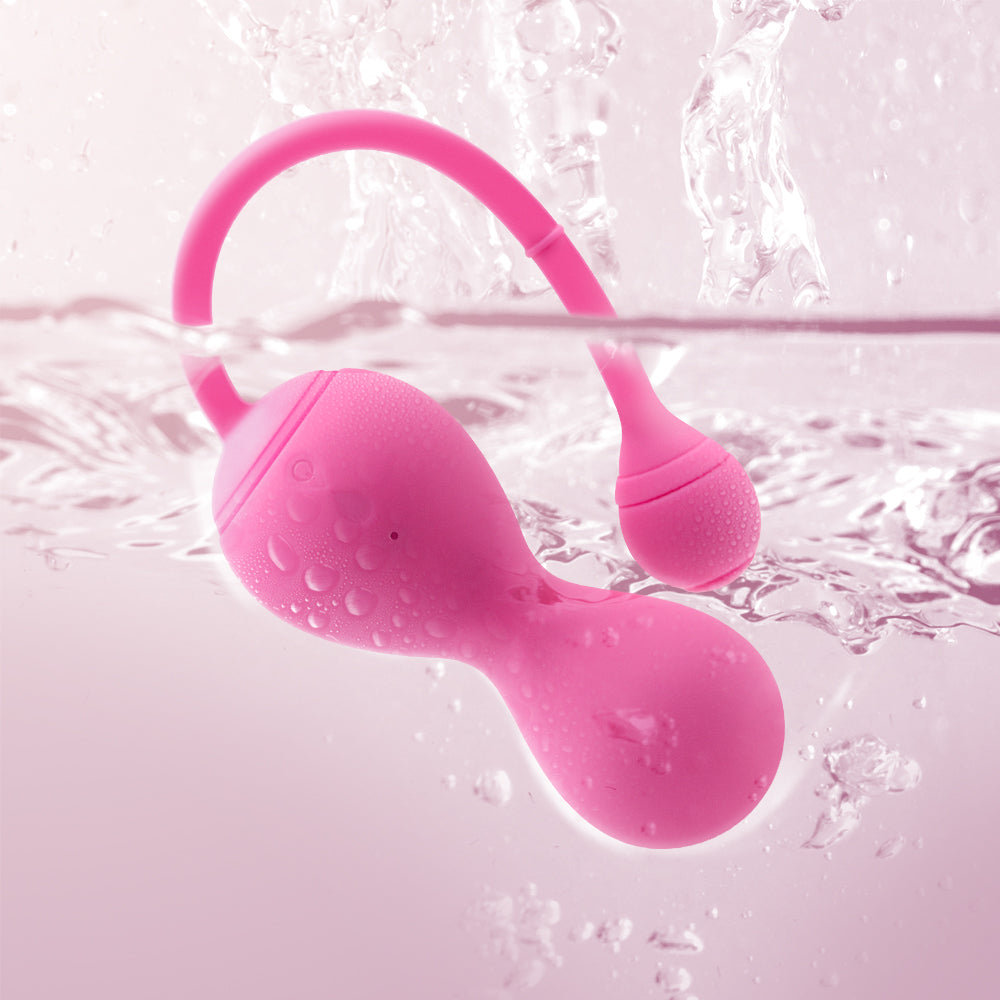 Pink silicone pelvic floor trainer with curved handle, water droplets on surface