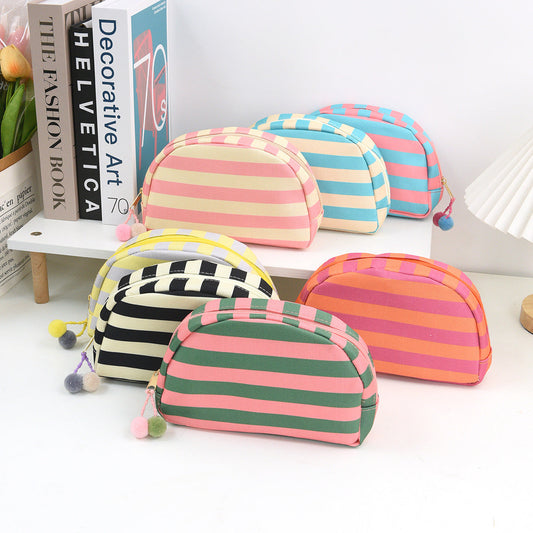 Striped shell makeup bag set with pom-pom zipper pulls, multicolor horizontal stripes.