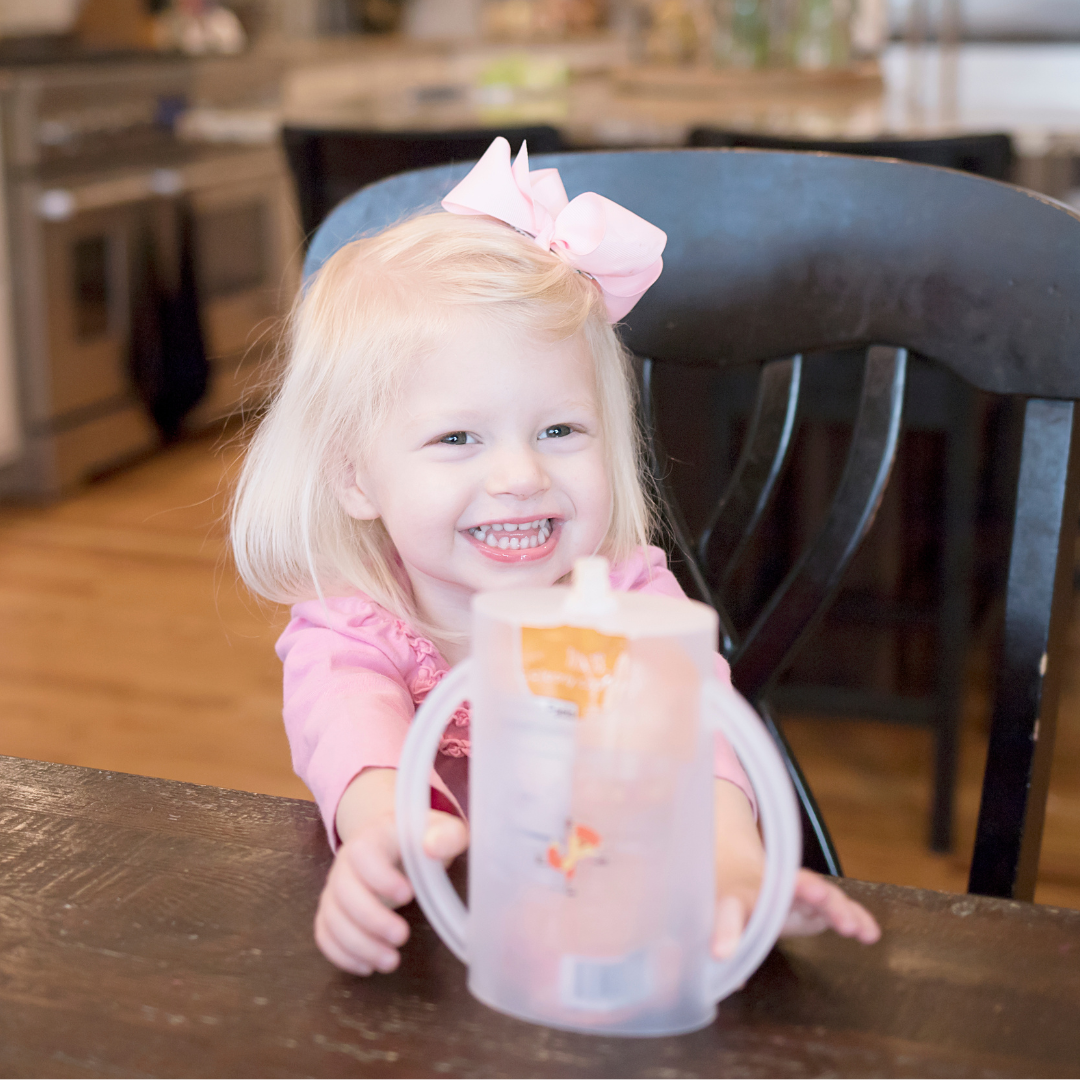 Clear flipping holder cup with handles being held by a smiling toddler