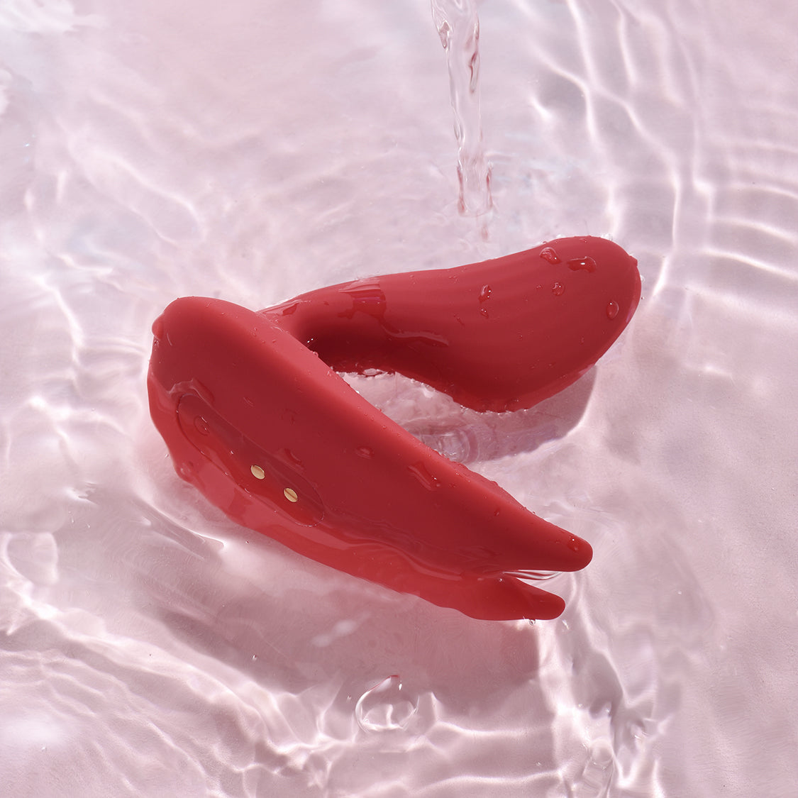 Red dual stimulation vibrator with two curved tips on wet surface