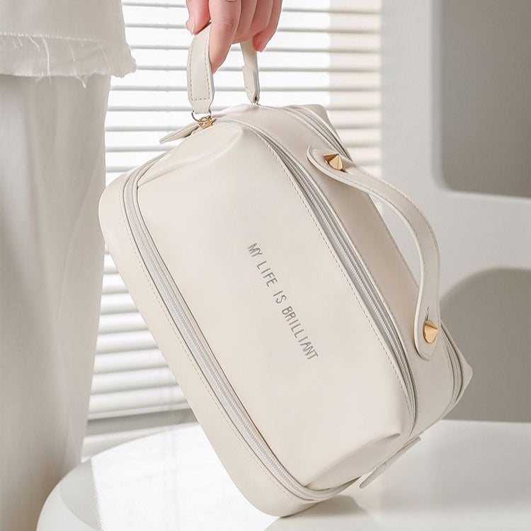 Off-white double-zip makeup bag held by top handle, slim sides and front zipper