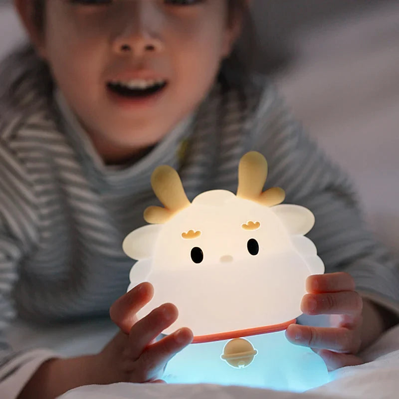 White dragon night light with warm glow, held by a child with orange cord
