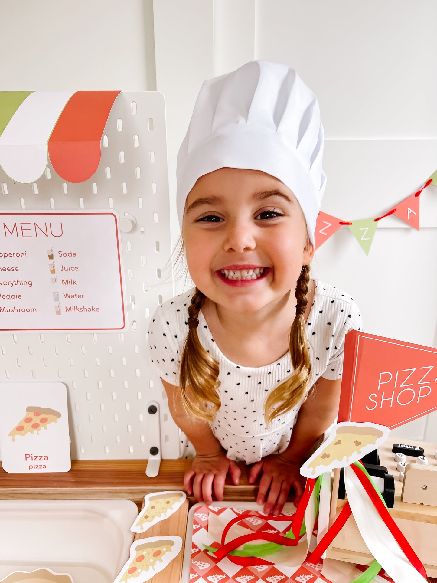 Pizza shop play kit with menu board, child in chef hat, and red pizza shop sign