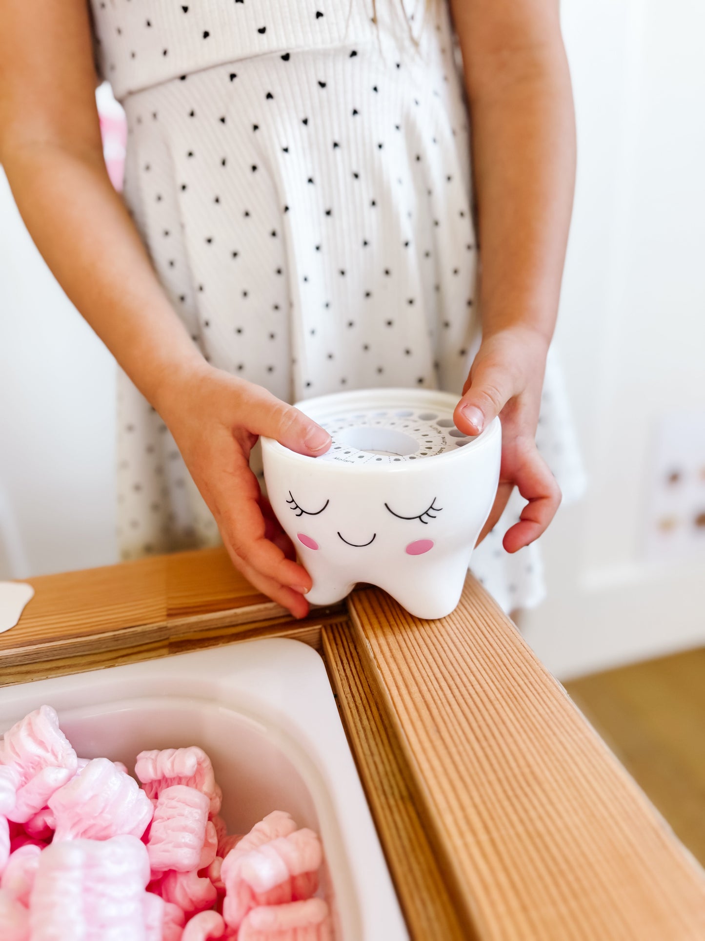Tooth-shaped ceramic container with smiling face being placed on a wooden tray
