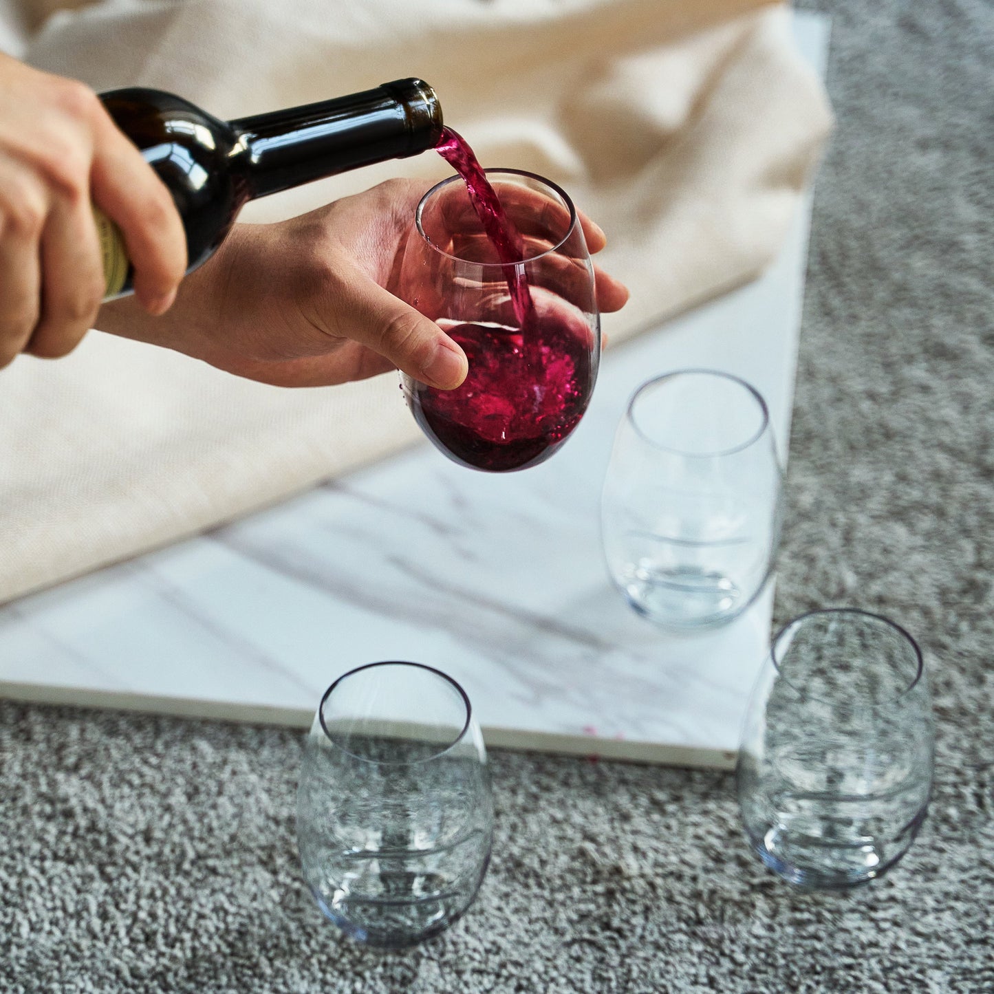 Stemless finger-indent wine glass being filled, clear acrylic, with red wine